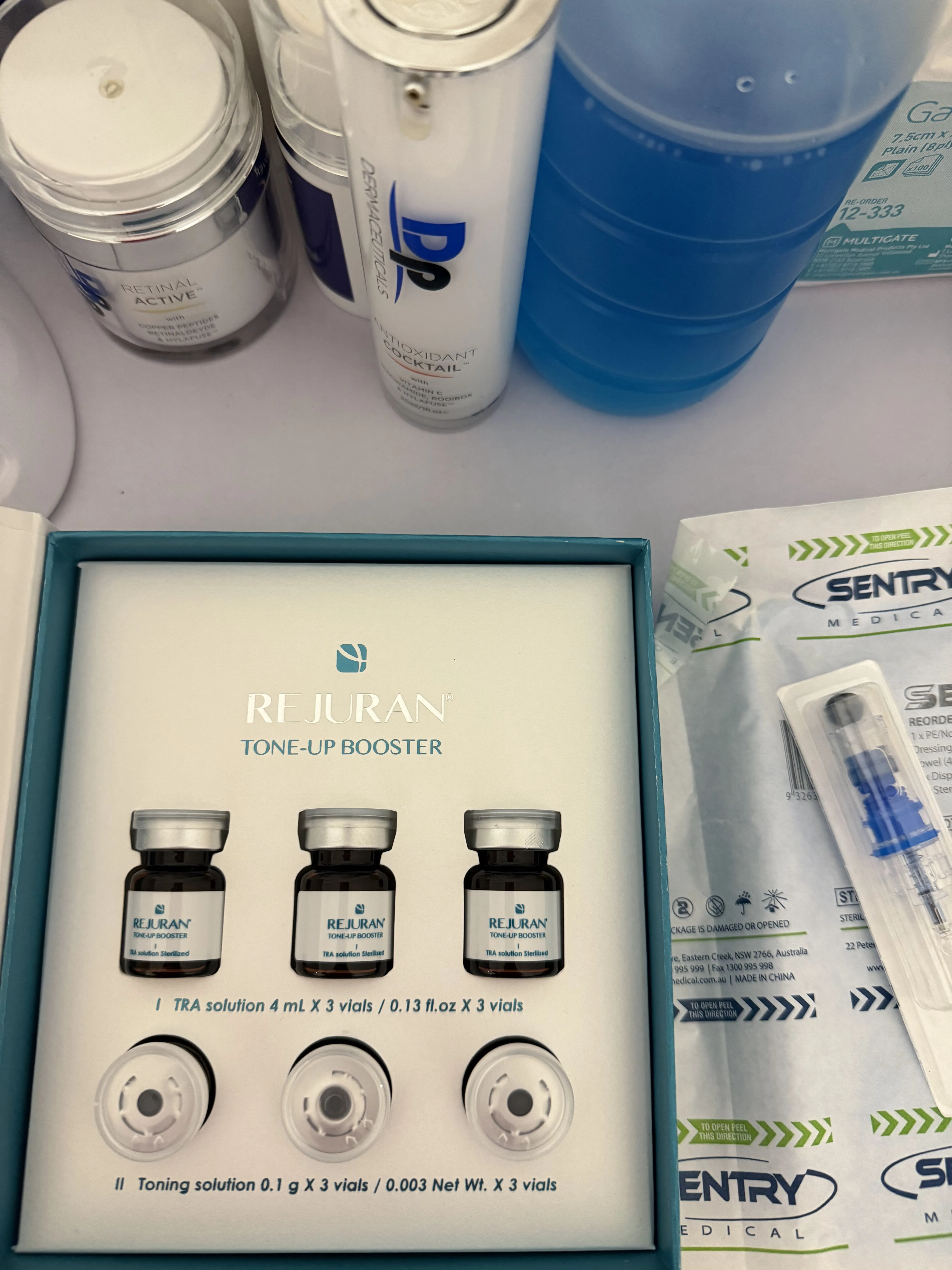 Flatlay of Rejuran Tone-Up Booster kit, DP actives and Sentry needles arranged on the treatment cloth