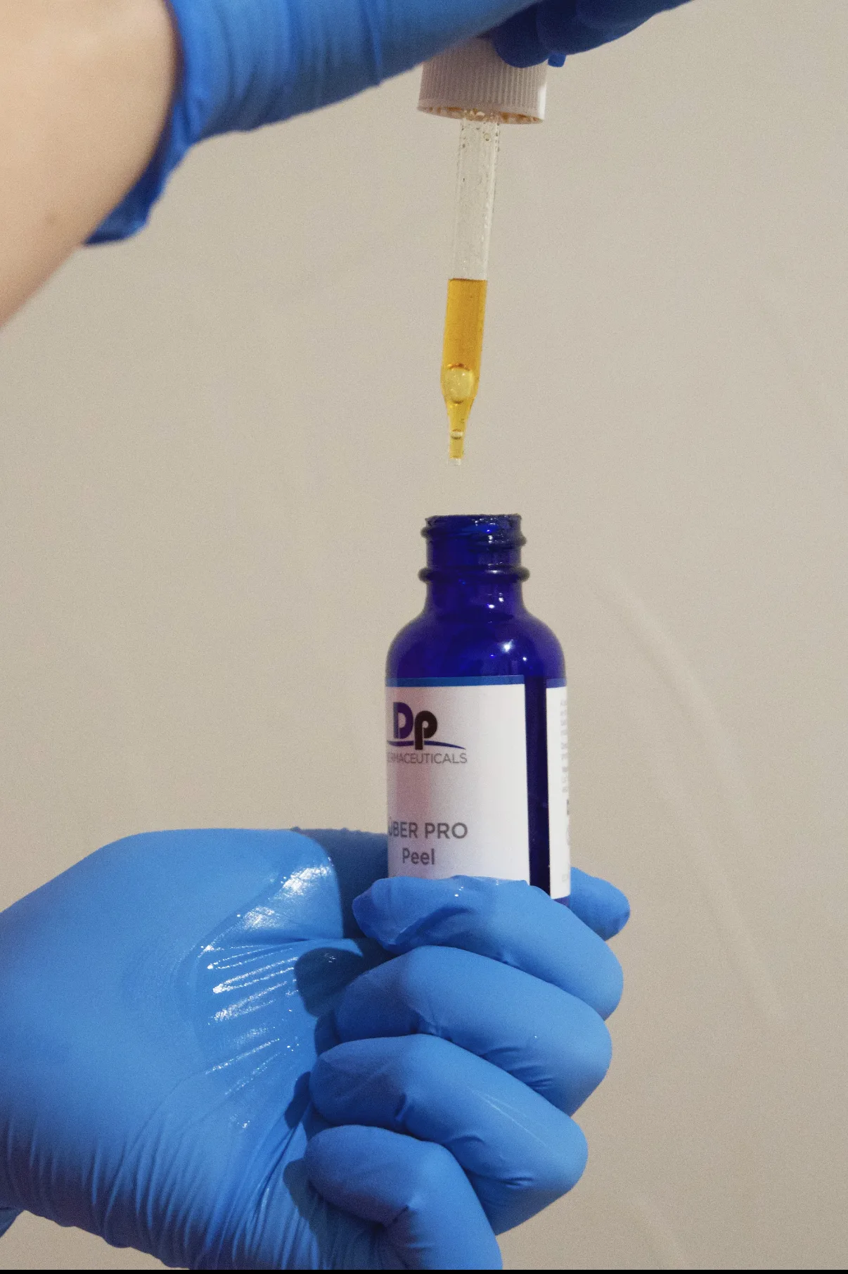 Blue-gloved hand holding a DP Dermaceuticals Über Pro Peel dropper, amber serum dripping