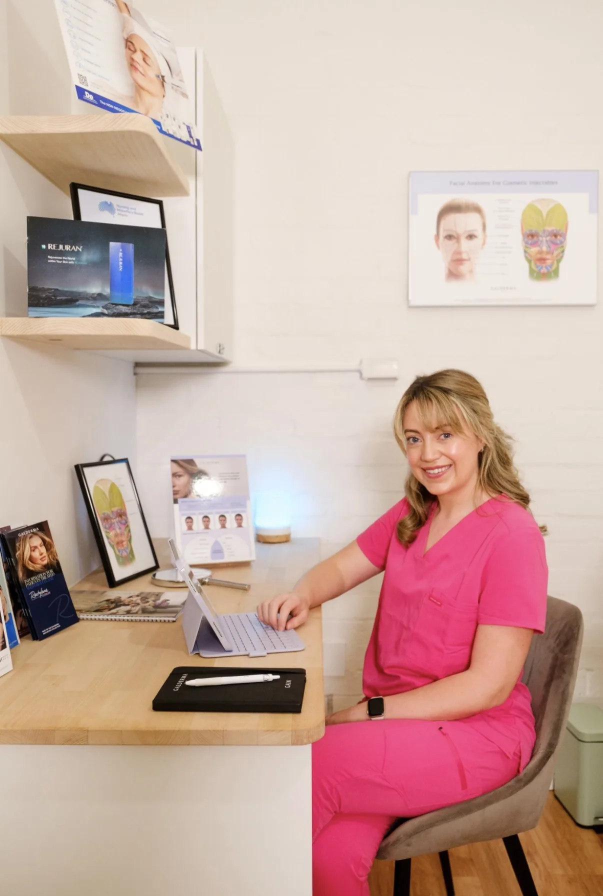 Nurse Cliodhna seated at her consultation desk with product shelving and anatomy poster behind her